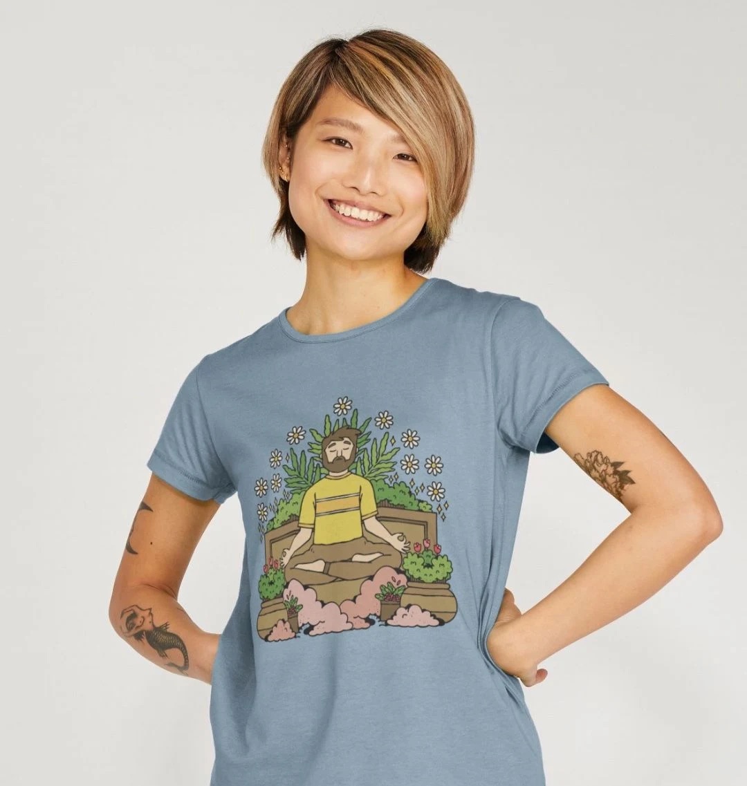 Model wearing a light blue t-shirt with an illustration across the chest. The illustration features a person in a meditation pose surrounded by plants.